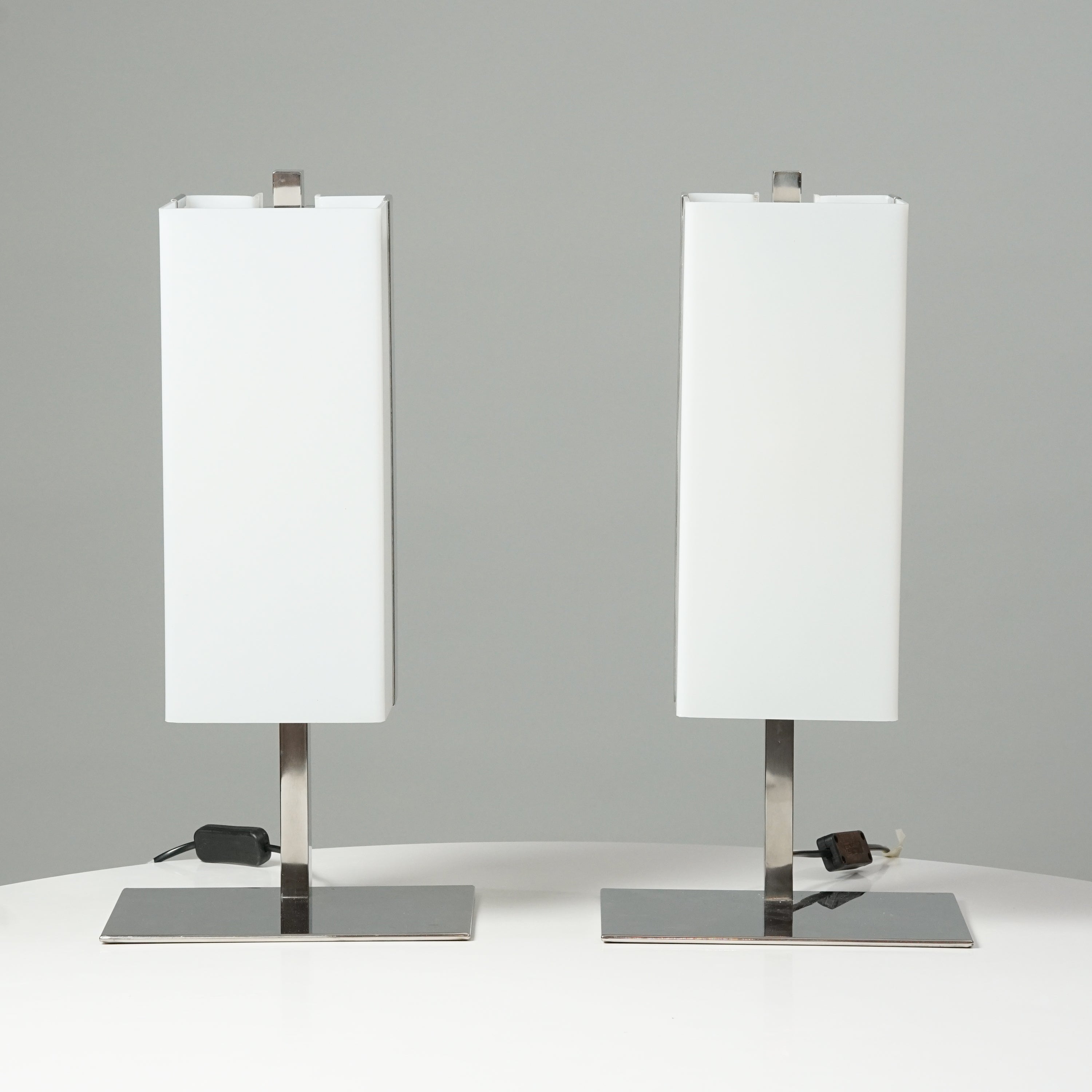 Two identical lamps. The shape of the white acrylic shade is of a rectangle and the base of the lamp is made of metal.